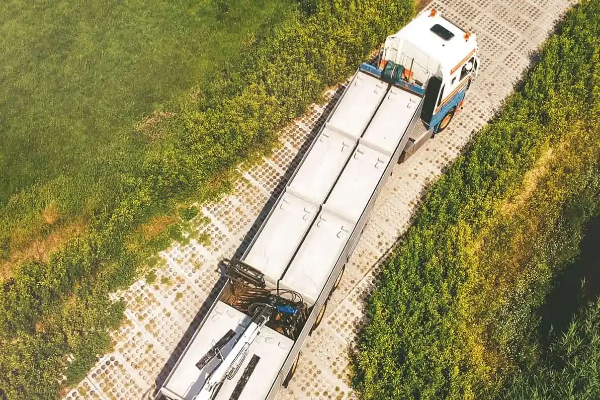 SIMbeton-vrachtwagen met kraan lost betonplaten op een kavelpad, gezien vanuit de lucht